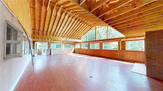 interior space with wood walls, plenty of natural light, vaulted ceiling, and hardwood / wood-style flooring