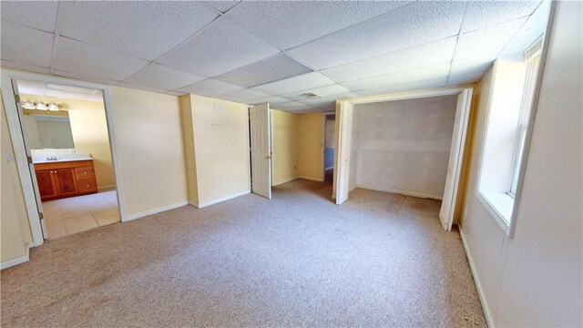 unfurnished bedroom with a paneled ceiling, light carpet, sink, and ensuite bathroom