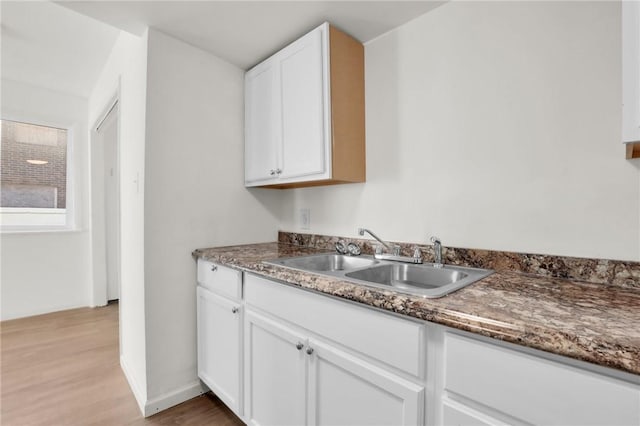 kitchen with dark stone countertops, white cabinetry, sink, and light hardwood / wood-style flooring