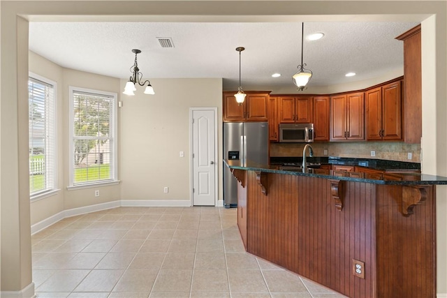 kitchen with brown cabinetry, decorative backsplash, a kitchen breakfast bar, dark stone counters, and appliances with stainless steel finishes