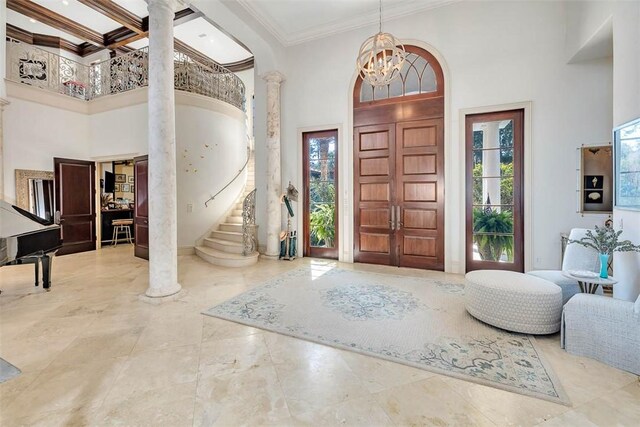 foyer entrance with a notable chandelier, a towering ceiling, ornamental molding, and decorative columns