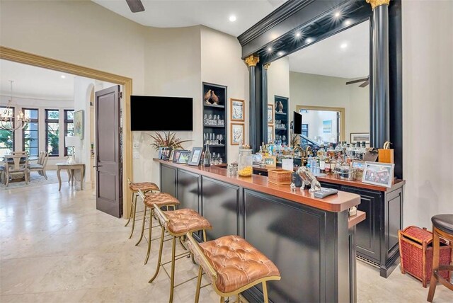 bar with crown molding, wooden counters, and ceiling fan with notable chandelier