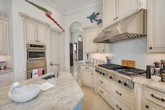 kitchen with sink, stainless steel appliances, light stone counters, crown molding, and cream cabinetry