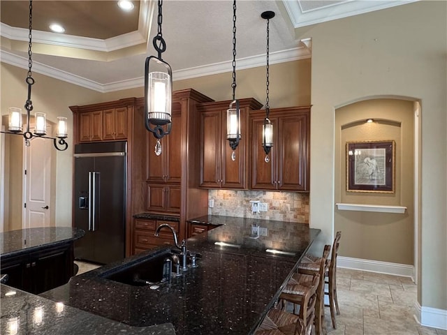 kitchen featuring ornamental molding, sink, decorative light fixtures, dark stone countertops, and built in fridge