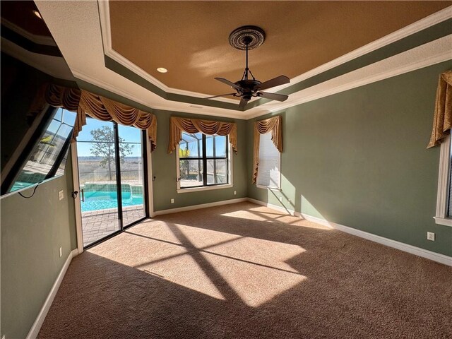 empty room featuring a tray ceiling, ceiling fan, ornamental molding, and light colored carpet