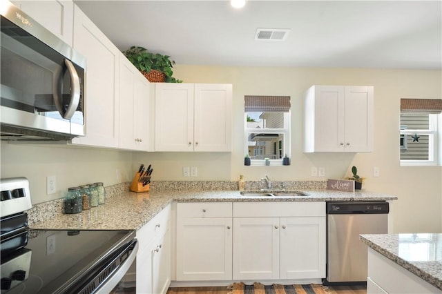 kitchen featuring stainless steel appliances, a sink, white cabinets, light stone counters, and healthy amount of natural light