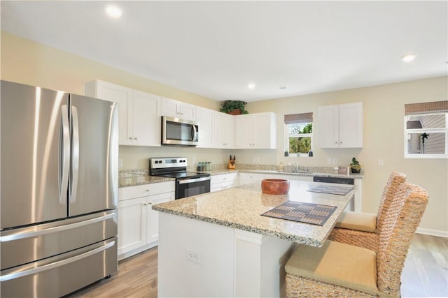 kitchen featuring appliances with stainless steel finishes, light wood-style floors, a center island, a breakfast bar area, and recessed lighting
