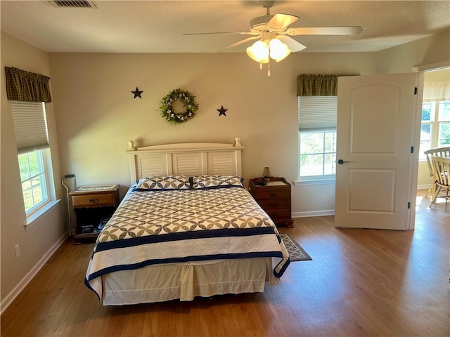 bedroom featuring ceiling fan, visible vents, baseboards, and wood finished floors