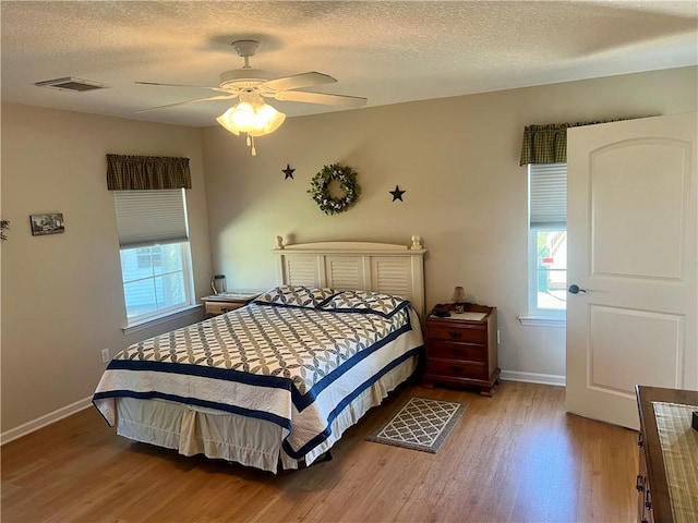 bedroom with a ceiling fan, wood finished floors, visible vents, baseboards, and a textured ceiling