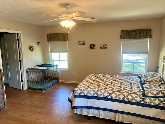 bedroom with a ceiling fan, wood finished floors, baseboards, and a textured ceiling