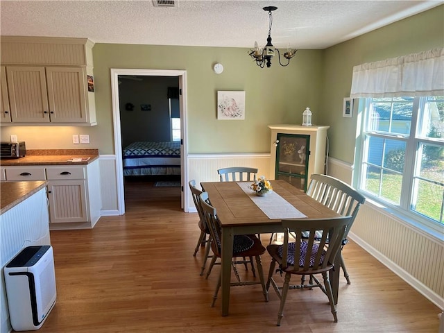 dining room featuring a textured ceiling, a notable chandelier, light wood finished floors, and wainscoting