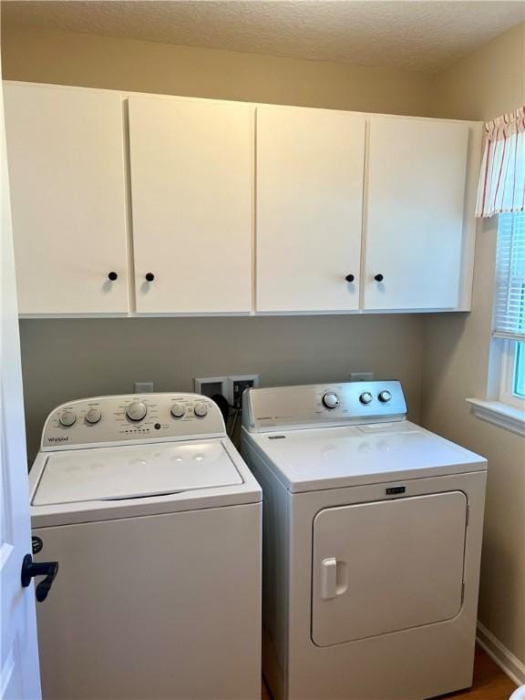 clothes washing area featuring a textured ceiling, cabinet space, and washing machine and clothes dryer