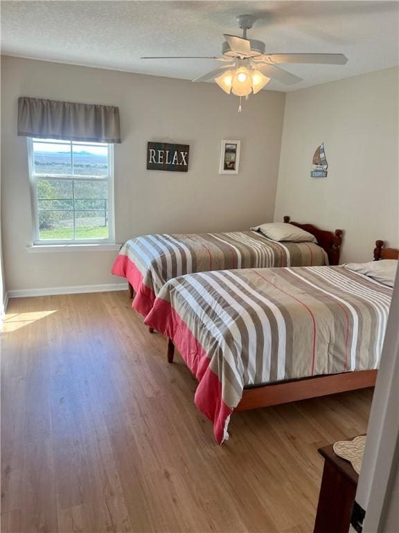 bedroom with ceiling fan, wood finished floors, baseboards, and a textured ceiling