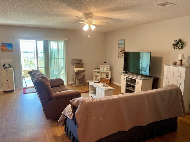 living area featuring baseboards, visible vents, a textured ceiling, and light wood-style floors