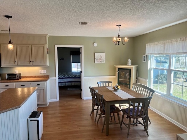 dining room featuring wood finished floors, a healthy amount of sunlight, visible vents, and wainscoting