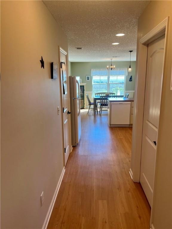 hall with an inviting chandelier, baseboards, light wood finished floors, and a textured ceiling