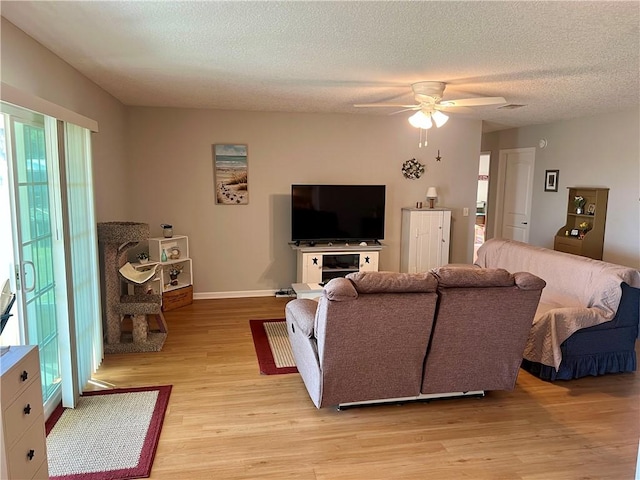 living room with light wood-type flooring, visible vents, a textured ceiling, baseboards, and ceiling fan