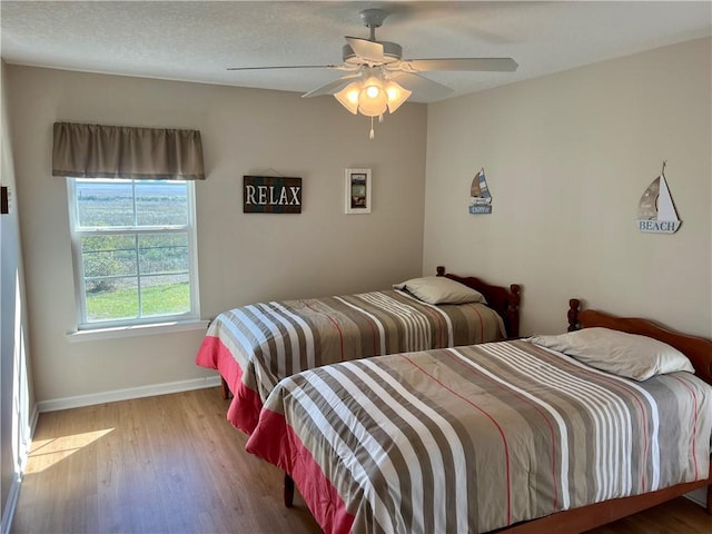 bedroom featuring ceiling fan, baseboards, a textured ceiling, and wood finished floors