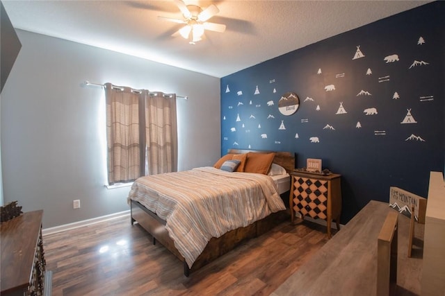 bedroom with baseboards, a ceiling fan, an accent wall, wood finished floors, and a textured ceiling