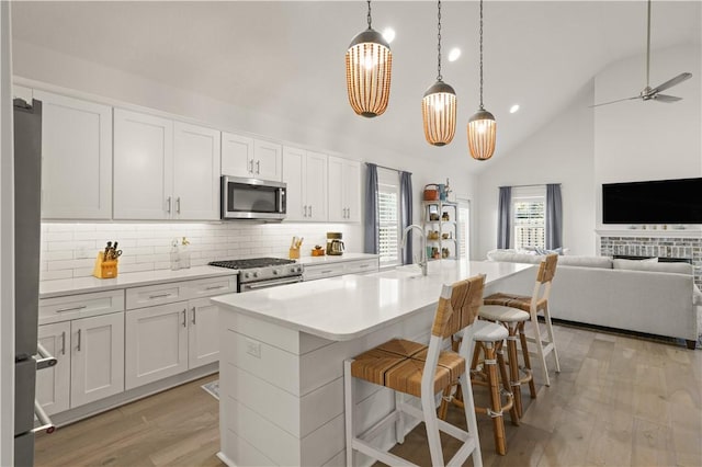 kitchen with sink, white cabinetry, an island with sink, decorative backsplash, and appliances with stainless steel finishes