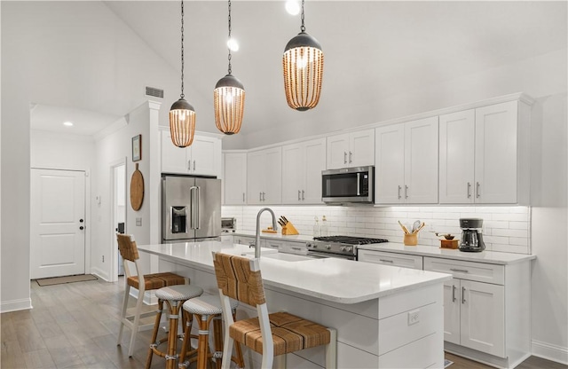 kitchen featuring high end appliances, pendant lighting, a center island with sink, white cabinetry, and sink