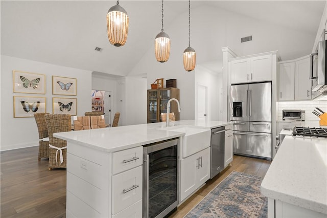 kitchen with hanging light fixtures, stainless steel appliances, an island with sink, wine cooler, and white cabinetry