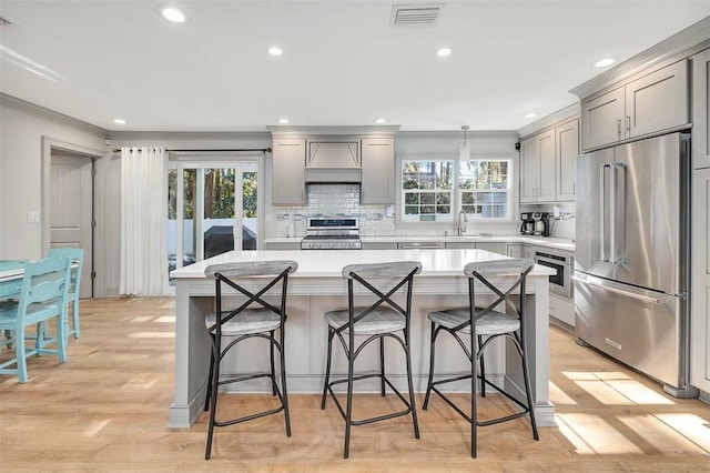 kitchen featuring a breakfast bar area, gray cabinets, a kitchen island, custom range hood, and appliances with stainless steel finishes