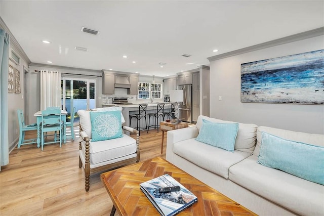 living room featuring light wood-type flooring, ornamental molding, and sink