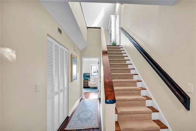 staircase with a high ceiling, wood finished floors, visible vents, and baseboards