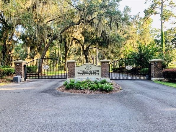 community / neighborhood sign featuring a gate and aphalt driveway