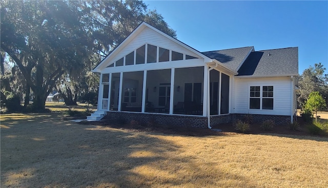 rear view of property featuring a yard, roof with shingles, and a sunroom