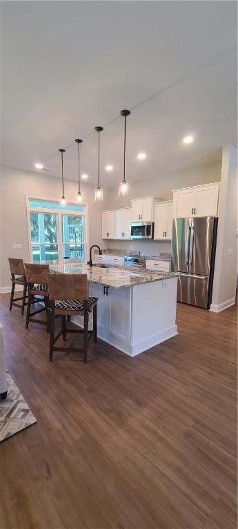 kitchen with appliances with stainless steel finishes, white cabinetry, an island with sink, and light stone countertops