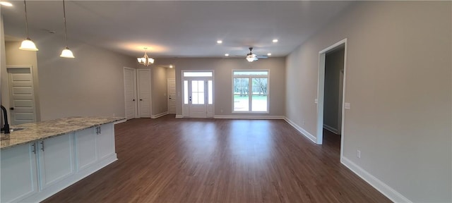 unfurnished living room featuring dark wood-style flooring, recessed lighting, a sink, baseboards, and ceiling fan with notable chandelier