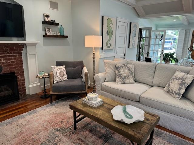 living room featuring wood-type flooring, a brick fireplace, beamed ceiling, and coffered ceiling