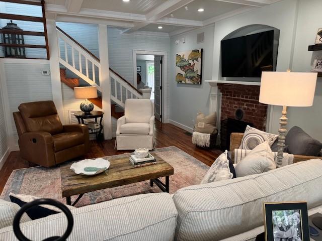 living room with dark hardwood / wood-style floors, coffered ceiling, a brick fireplace, and beamed ceiling