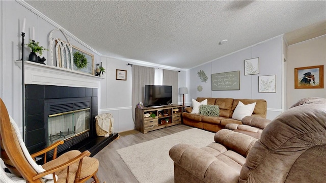 living room featuring a textured ceiling, crown molding, a fireplace, vaulted ceiling, and light wood-style flooring