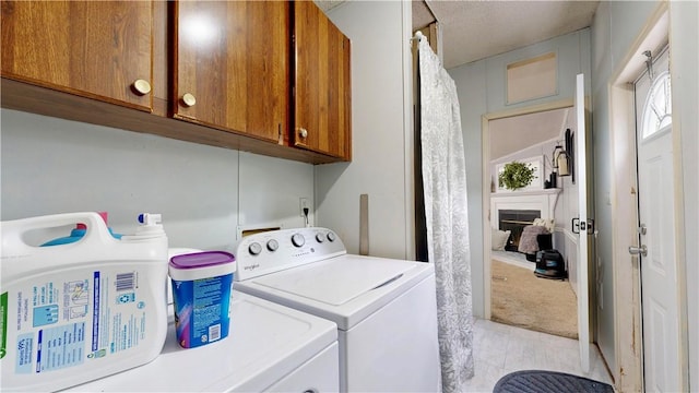 laundry room with washing machine and clothes dryer, a fireplace, cabinet space, light tile patterned floors, and light carpet