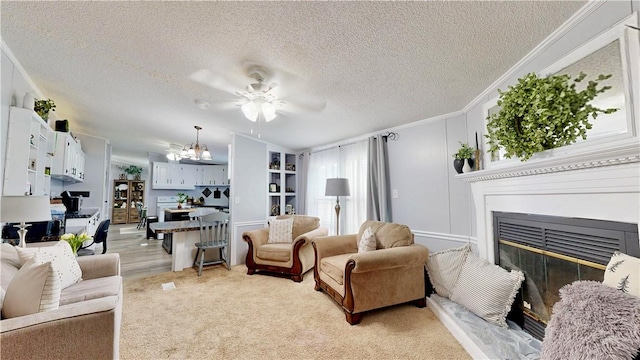 living room with a textured ceiling, a glass covered fireplace, ornamental molding, and ceiling fan with notable chandelier