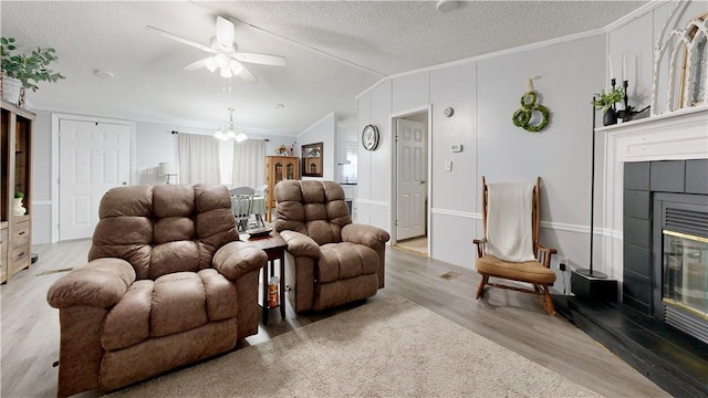 living room featuring a textured ceiling, ornamental molding, light wood finished floors, and a tile fireplace