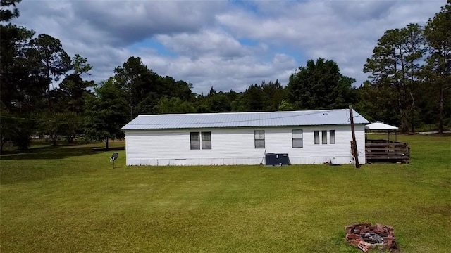 rear view of property with central AC unit, a yard, and metal roof