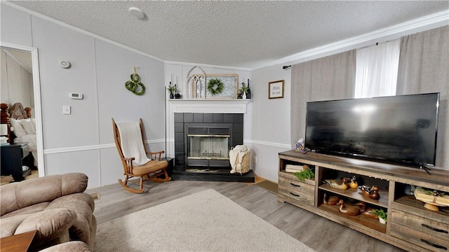 living room with a textured ceiling, ornamental molding, wood finished floors, and a fireplace