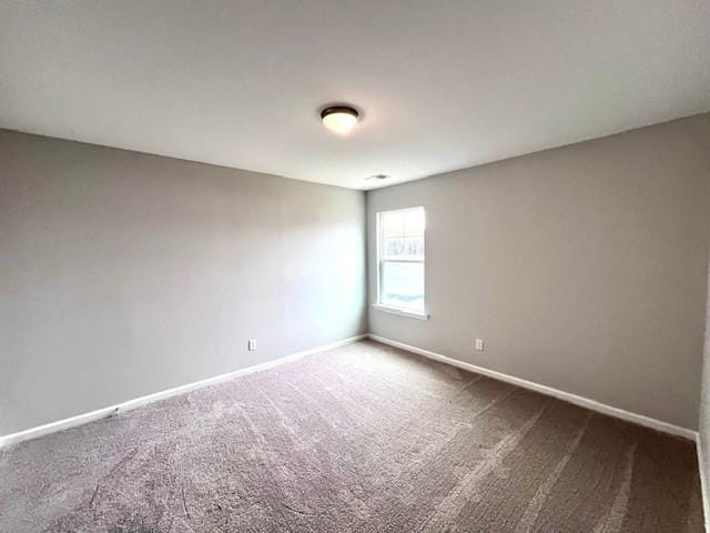 spare room with baseboards and dark colored carpet