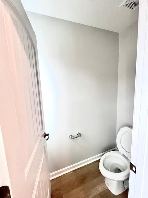 bathroom featuring toilet, wood finished floors, visible vents, and baseboards