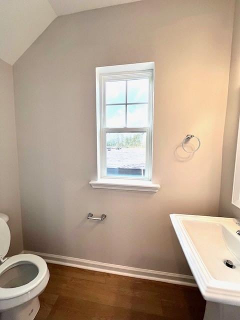 half bathroom with toilet, a sink, wood finished floors, baseboards, and vaulted ceiling