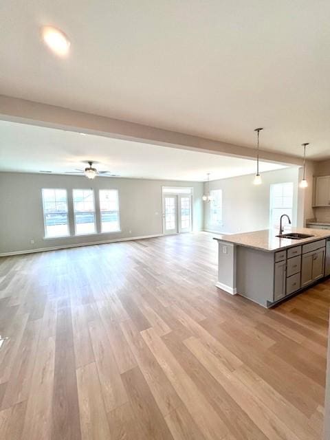 kitchen featuring open floor plan, an island with sink, light wood-type flooring, light countertops, and a sink