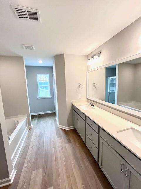 bathroom with visible vents, double vanity, wood finished floors, a bath, and a sink