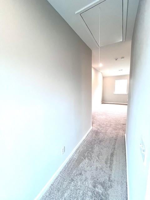 hallway featuring attic access, carpet, and baseboards