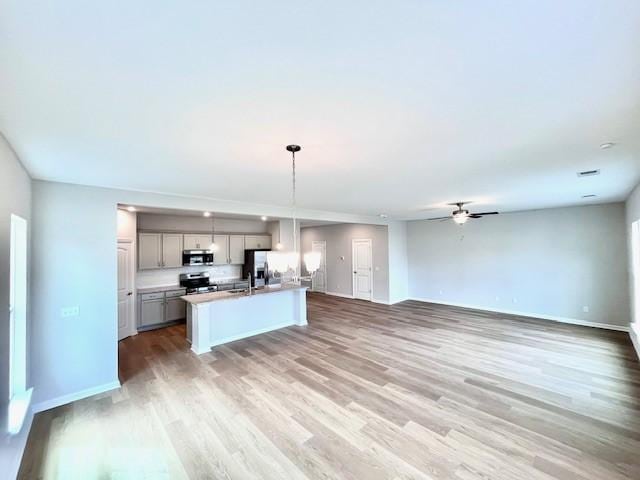 kitchen featuring light wood finished floors, open floor plan, an island with sink, gray cabinets, and appliances with stainless steel finishes