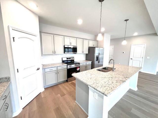 kitchen featuring a sink, light stone counters, light wood-style flooring, appliances with stainless steel finishes, and a kitchen island with sink