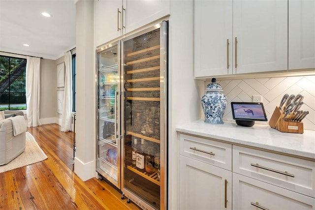 interior space with white cabinetry, beverage cooler, light stone counters, backsplash, and light hardwood / wood-style floors